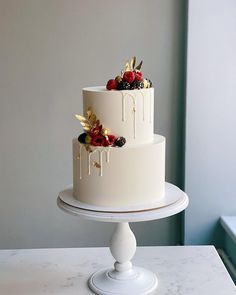 a three tiered cake with berries and gold leaf decorations on top sits on a white pedestal