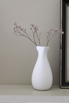 a white vase sitting on top of a shelf next to a framed photo and a black frame