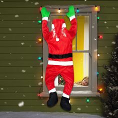 a man dressed as santa claus hanging from a window in front of a christmas tree