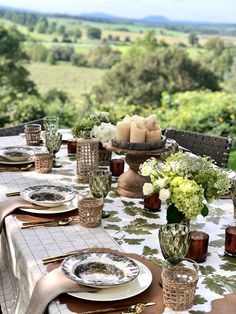 an outdoor table set with place settings and flowers in vases on top of it