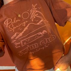 "Having a SWELL-tering time in Palm Springs! Inspired by Palm Springs pool culture and vintage motel matchbooks given out in the 60s & 70s, hand drawn by us as always! 100% natural cotton, pigment dyed unisex tee achieves a vintage lived-in look. Printed with salmon water based ink on a burnt sienna unisex boyfriend tee. Hello monochromatic moment! Unisex tee runs one size larger for women. Model is 5'6\" size 7 wearing a Medium tucked for an oversized look. Wash cold and tumble dry low to s Palm Springs Bach, Palm Springs Vintage, Icelandic Poppies, Bible Shirts, 70s Clothing, California Shirt, 70s Shirts, Vintage Outdoor, Tee Tree