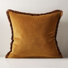 a brown pillow with fringe trim on the front and back of it, sitting on a white surface