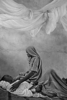 an old black and white photo of a woman sitting on a bed next to a baby