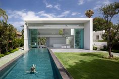 a pool in the middle of a yard with grass and trees around it, next to a large white house