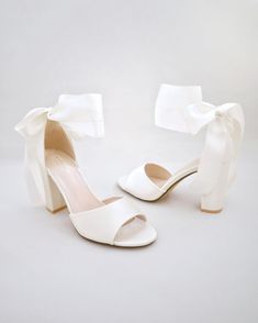 a pair of white high heeled shoes with a bow