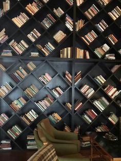 a living room filled with lots of books on black shelves next to a green chair