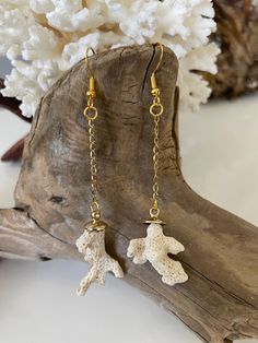 a pair of earrings with gold chains hanging from it's ear hooks, sitting on top of a piece of driftwood