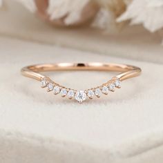 a rose gold wedding band with five diamonds on the side, and a white flower in the background