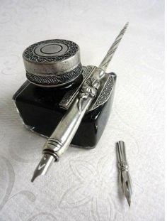 a fountain pen sitting on top of a desk next to an ink container and two pens