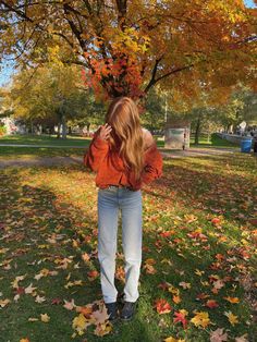 a woman standing under a tree with leaves on the ground