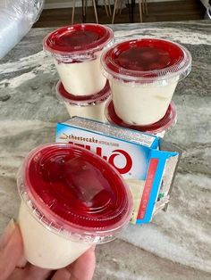 three plastic cups with yogurt in them sitting on a counter next to a box of cheesecakes