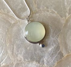 This pendant features a natural, round, Green Serpentine gemstone. This particular gemstone has natural, white, polkadot, inclusions that set it apart from the other gemstones. I knew I had to work with it 🥰 The semi-translucent nature and soft green color inspired me to make a simple but unique setting! I began by using a plain, silver, bezel wire, to secure the stone. Then, I attached a medium-size, plain, round, wire to frame part the stone, altering the silhouette of the stone just a bit. Then, I added a small piece of plain, round wire to fit against the other piece of plain wire. I did this to further alter the silhouette. Next, I added a flattened, sterling silver granule to the bottom of the piece. Lastly, I created a single, "V" bale (5mm), allowing for a variety of chains to be Chalcedony Natural Stone Round Necklaces, Chalcedony Necklaces With Natural Stones, Jade Cabochon Round Pendant Necklace, Round Jade Cabochon Pendant Necklace, Round Jade Cabochon Necklace, Round Chalcedony Necklace Gift, Handmade Round Chalcedony Necklace, Unique Round Chalcedony Necklace, Bezel Wire