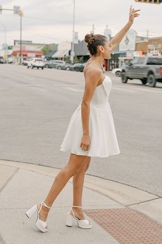 a woman in a white dress is crossing the street with her hand up to stop