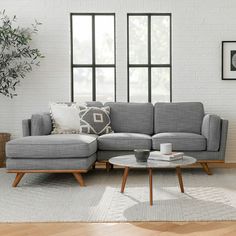 a living room with gray couches and white brick walls, coffee table and potted plant