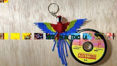 a colorful bird keychain hanging on a wooden wall next to a dvd disc