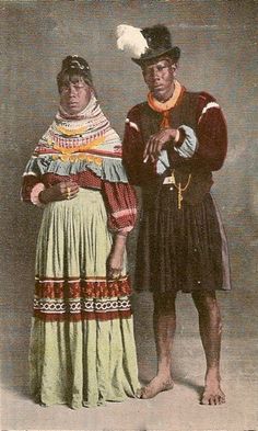 an old photo of two people standing next to each other in native american clothing and hats