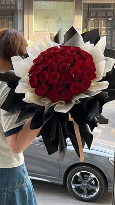 a woman holding a large bouquet of red roses in front of a car on the street