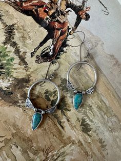 a pair of earrings sitting on top of a rock next to a drawing of a man riding a horse