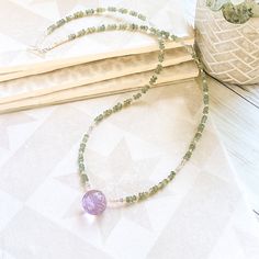 a necklace with green beads and a purple bead is sitting on a table next to a potted plant