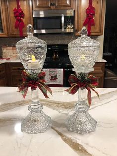 two clear glass candlesticks with bows on them sitting on a marble counter top