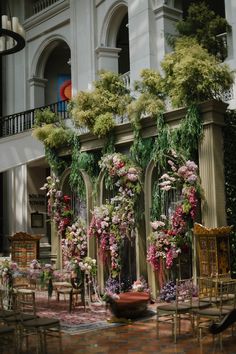 an outdoor wedding setup with flowers and greenery on the wall, surrounded by chairs