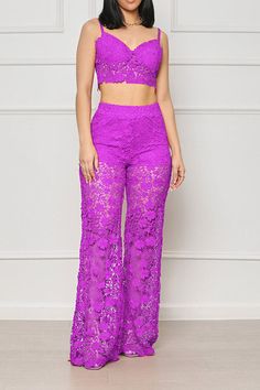 a woman standing in front of a white wall wearing purple lace pants and crop top