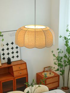 a lamp hanging over a dining room table next to a potted plant and dresser