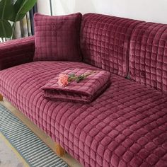 a red velvet couch sitting on top of a wooden floor next to a potted plant