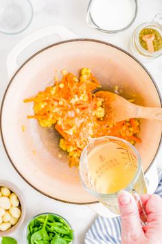 someone is pouring something into a bowl with vegetables and other ingredients in bowls around it