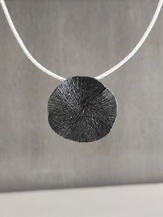 "This round pendant necklace is a stunning and unique handmade piece of 925 sterling silver. The pendant is designed in the shape of a wavy circle with an engraving on its surface and is passed on a white silk cord with a handmade hook clasp, you can choose a different color as shown in the photo black, red, gray. A black and white statement necklace for all time classic looks! DESCRIPTIONS and MEASUREMENTS: Materials: Oxidized sterling silver. Diameter:approx 3,4 (cm) 1,34 (in)\". Length cord: 41,0 (cm) 16,14 (in)\". SEE MORE NECKLACES HERE: www.etsy.com/shop/ArtisJewels?ref=seller-platform-mcnav§ion_id=35815722 Visit my Etsy shop, ArtisJewels, to see more necklaces and jewelry and other unique handmade pieces. www.etsy.com/shop/ArtisJewels Do not hesitate to contact me for any questions Unique Black Oval Pendant Necklace, Sterling Silver Coin Pendant Jewelry, Silver Jewelry With Large Round Disc Pendant, Artisan Round Sterling Silver Necklace, Silver Necklace With Large Round Pendant, Handmade Minimalist Silver Necklace, Modern Hammered Round Necklace, Modern Engraved Round Pendant Necklace, Unique Jewelry With Oxidized Round Pendant