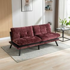 a red couch sitting on top of a wooden floor next to a glass coffee table