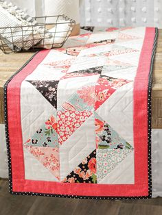 a quilted table runner on top of a wooden table next to a basket and vase