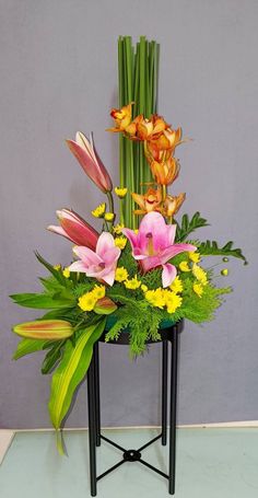 an arrangement of flowers is displayed on a small table with green grass and yellow flowers