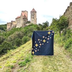 a quilted blanket sitting on top of a lush green hillside next to a castle