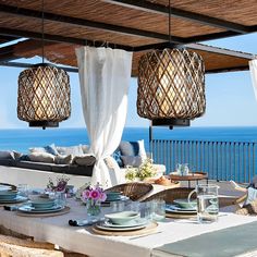 an outdoor dining area overlooking the ocean with wicker chairs and table set for four