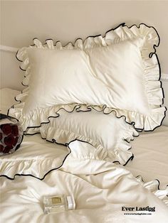 a bed with white sheets and black ruffles on the pillow cases, along with a red vase