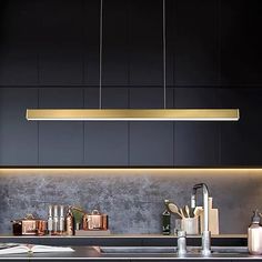 a modern kitchen with black cabinets and gold lighting above the countertop, along with copper utensils