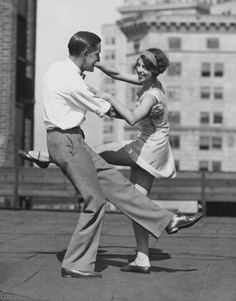 a man and woman are dancing on the sidewalk in front of tall buildings with their arms around each other