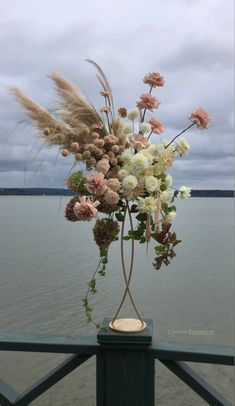 a vase filled with lots of flowers on top of a wooden table next to the water