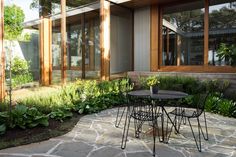 a table and chairs sitting on top of a stone patio next to plants in front of windows