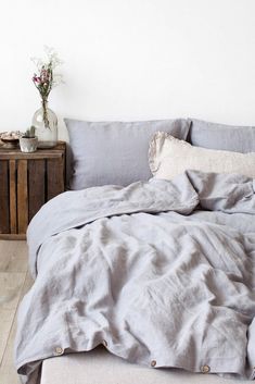 an unmade bed with grey linens and pillows