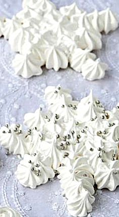 some white frosted cookies are on a lace tablecloth and one is decorated with silver beads