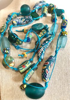 A beautiful combination of Ghana Krobo beads are hand-knotted to create this long necklace.  It is a one-of-a-kind piece. -  Handmade, one-of-a-kind. -  Lovely combination of teal and yellow Ghana Krobo beads, sandcast, fused glass, ceramic, and recycled glass beads. -  The hand-knotting and spacing allows for each bead to be individually showcased. -  Necklace measures 36" in length and is not adjustable. -  Beads are strung on teal hemp cord. -  Brass "hand made" charm tag. -  Comes with jewel Unique Recycled Glass Necklaces For Beach, Unique Recycled Glass Beach Necklace, Bohemian Hand-strung Beaded Necklaces For Beach, Handmade Green Bohemian Beaded Necklaces, Hippie Hand-strung Beads For Beach, Handmade Round Beads Long Necklace For Festival, Hippie Style Green Beaded Necklace For Festivals, Handmade Long Necklace With Round Beads For Festivals, Artisan Green Beaded Necklace For Festivals