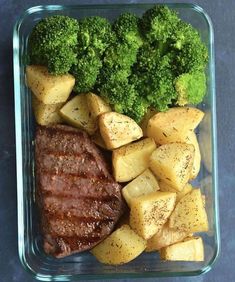 a glass container filled with broccoli and potatoes next to meat on the side