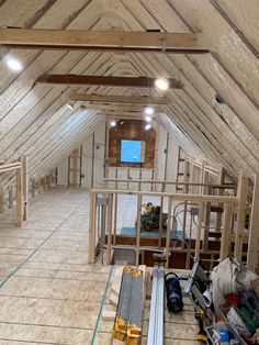 an unfinished attic with wooden beams and exposed ceilinging, including two television screens on the wall