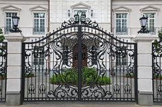 an ornate iron gate in front of a large white building with two black doors and windows