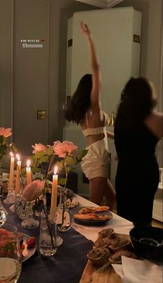 two women standing in front of a table with food and candles on top of it