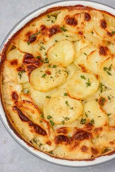 a dish with potatoes and parsley in it on a gray table top next to a wooden utensil