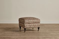 an upholstered footstool on the floor in front of a white wall