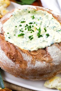 a bread bowl filled with cream cheese and chives on a plate next to crackers